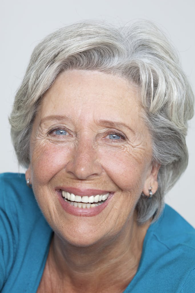 Close-up portrait of a smiling senior woman with grey hair in a studio setting.
