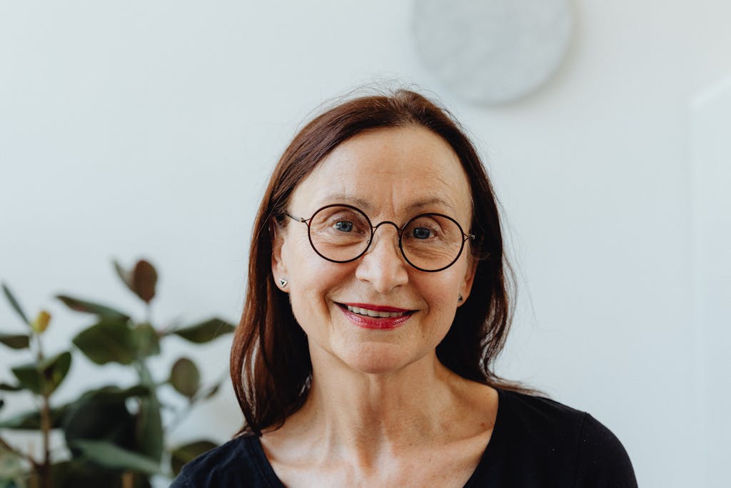 Portrait of a smiling senior woman wearing glasses against a bright indoor background.